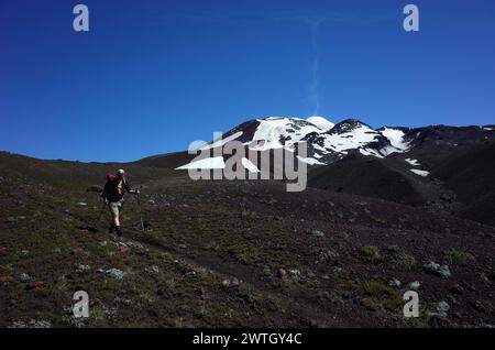 Escursionista sul paesaggio scuro del vulcano Villarrica Traverse Trail, cielo azzurro, Parco Nazionale Villarrica, attività all'aperto in Cile, Ecoturismo in Foto Stock