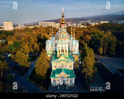 Vista aerea con droni della Cattedrale dell'Ascensione, chiesa ortodossa russa e montagne innevate sullo sfondo del Parco Panfilov, con il cielo del tramonto ad Almaty ci Foto Stock