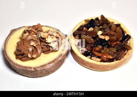 Due torte rotonde a forma di cestini con massa di cagliata, decorate con rosette di panna e uva passa su sfondo bianco. Foto Stock