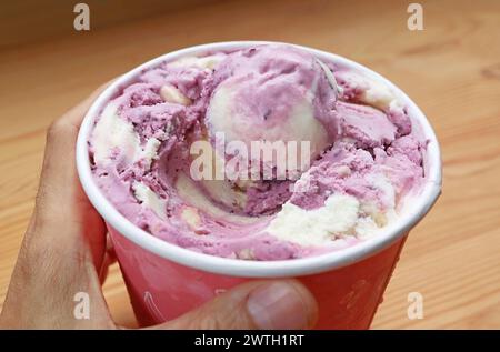 Tenere a mano una tazza di gelato allo yogurt ai mirtilli su un tavolo di legno Foto Stock
