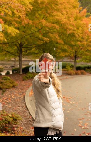 donna che tiene in mano foglie d'autunno che cambia foglie su una strada vuota Foto Stock