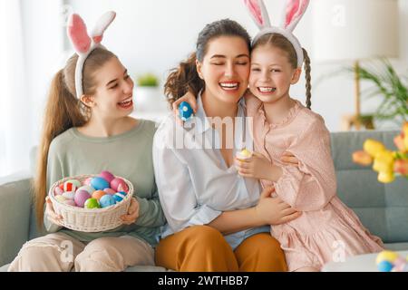 Buona vacanza. Madre e le sue figlie con uova da pittura. La famiglia festeggia la Pasqua. Le ragazze cute dei bambini stanno portando le orecchie conigliate. Foto Stock