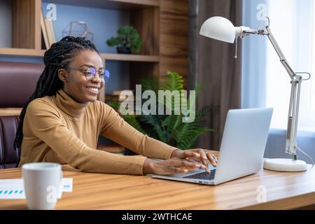 Professionale in occhiali con dreadlock, lavora online dall'ufficio domestico Foto Stock