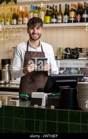 Barman barman barman in piedi con un tablet digitale al bancone del bar Foto Stock