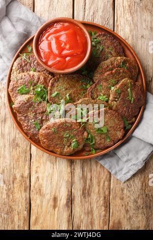 Polpettine di fegato di manzo fritte servite con salsa di pomodoro ed erbe da vicino in un piatto sul tavolo. Vista dall'alto verticale Foto Stock