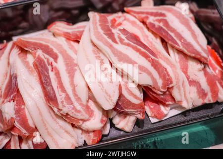 Strato di pancetta di lardo vari tagli di bistecche di maiale, diverse parti del corpo tagliano la carne in vendita in contenitori su un banco del negozio Foto Stock