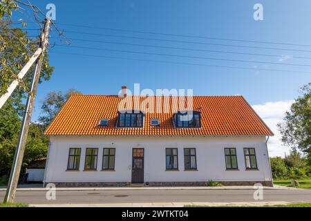 Casa bianca con tegole rosse e cavi elettrici sospesi lungo la strada sull'isola di Livø, Limfjord, Nordjylland, Danimarca Foto Stock