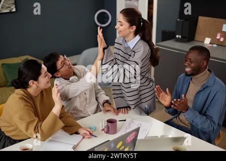 Gruppo multietnico di persone alto cinque durante riunioni di lavoro di successo in ufficio e festeggiamenti Foto Stock