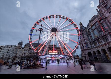 Anversa, Belgio, 25 gennaio 2024, al calare del crepuscolo, la ruota panoramica diventa un punto focale radioso nel vivace paesaggio urbano di Anversa. Le sue luci vivaci aggiungono un contrasto giocoso e moderno all'architettura classica che circonda la piazza. La lunga esposizione crea striature di luce, catturando la ruota panoramica in movimento e la sfocatura di pedoni e ciclisti, aggiungendo un senso del ritmo e del flusso della città. The View, la ruota panoramica nel paesaggio urbano serale di Anversa. Foto di alta qualità Foto Stock