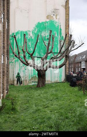 Londra, Regno Unito, 18 marzo 2024. I visitatori si sono riuniti a Hornsey Street, vicino a Finsbury Park, a nord di Londra, per vedere il nuovo murale di Banksy. La vernice verde è stata spruzzata su un muro dietro l'albero per dare l'illusione di fogliame, con una persona che tiene un tubo flessibile a pressione stampigliato accanto ad esso. La vernice verde sembra assomigliare al colore della segnaletica del Consiglio di Islington, e c'è anche un possibile collegamento con il giorno di San Patrizio di ieri. Credito : Monica Wells/Alamy Live News Foto Stock