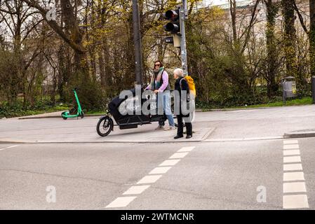 Monaco, Germania - marzo 3,2024, Una donna in sella a una bici cargo si ferma ad un incrocio Foto Stock