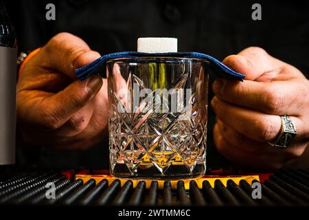 Mani di un barista che prepara un classico cocktail Absinthe, focalizzato su un cubetto di zucchero e amari, un passo essenziale nella mixologia. Foto Stock