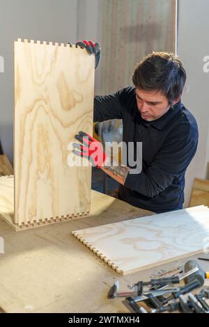 Falegname ispanico di mezza età che lavora in piedi nella sua falegnameria assemblando un pezzo di mobili Foto Stock