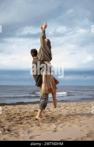 Un momento emozionante in cui una donna viene sollevata in aria da un uomo sulla spiaggia, che trasuda felicità e libertà, una perfetta cattura di un gioioso coupl Foto Stock