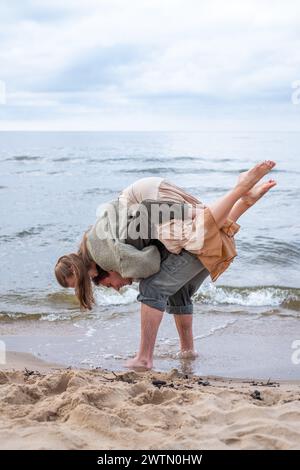 Un momento spontaneo sulla spiaggia, mentre un uomo porta giocosamente una donna sulla schiena, ridendo e godendosi un tempo spensierato al mare, temi di com Foto Stock