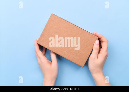 Mani che reggono una confezione regalo in carta artigianale con come regalo per Natale, Capodanno, san valentino o anniversario su sfondo blu, vista dall'alto. Foto Stock