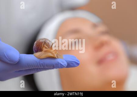 Procedura cosmetologica. Arachin lumaca sulla mano di un estetista, sullo sfondo una bella faccia di giovane donna Foto Stock