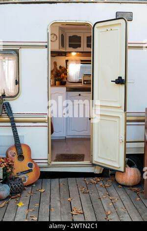 Portico per camper con mobili da giardino. Giardino autunnale arredato. Campeggio in giardino. Ingresso in rimorchio con chitarra e zucca sul rimorchio per roulotte in terrazza. Foto Stock