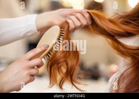 Parrucchiere pettinando i lunghi capelli rossi del suo cliente nel salone di bellezza. Cura professionale dei capelli e creazione di acconciature. Foto Stock