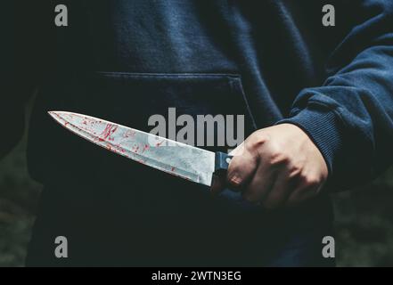 Un uomo con un coltello sanguinoso in mano da vicino. Foto Stock