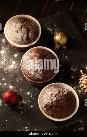 muffin al cioccolato con zucchero a velo su sfondo nero. Decorazione natalizia . Ancora vita da vicino. Foto del cibo Foto Stock