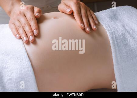 Una donna incinta che fa un massaggio termale con la mano sullo stomaco Foto Stock