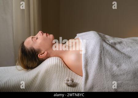 Una donna sdraiata sul lettino massaggiante, avvolta in un asciugamano bianco per il massimo comfort Foto Stock