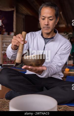 Un ritratto verticale di un latino multirazziale con caratteristiche asiatiche, con una ciotola cantante tibetana. La sua espressione riflette la serenità e il co spirituale Foto Stock