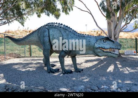 Cromwell, nuova Zelanda- 3 gennaio 2024: Statua realistica di dinosauro in posa a piedi a Highlands Park, Cromwell, nuova Zelanda, con alberi di gomma e grou di ciottoli Foto Stock