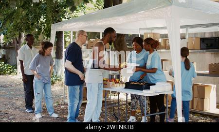 I volontari assistono i meno fortunati in una banca alimentare. Le donazioni di pasti sono distribuite da volontari in modo amichevole, esemplificando lo spirito della comunità e del lavoro caritatevole. Foto Stock