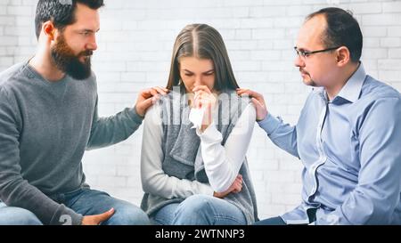 Membri del gruppo che sostengono la donna sconvolta vittima di violenza domestica durante la sessione di terapia Foto Stock