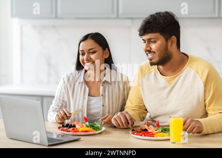 Una coppia indiana allegra fa colazione e guarda un film su un computer portatile Foto Stock