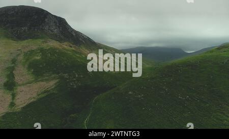 Vista aerea delle catene montuose scozzesi: Percorso tra verdi colline. Nuvole grigie avvolgono la cima dei supporti in estate. Natura selvaggia e incontaminata dell'isola di Arran. Riprese in 4K (UHD) Foto Stock