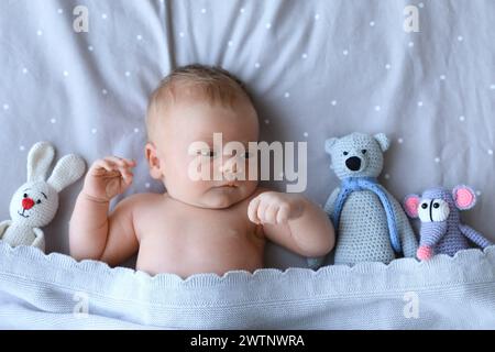 Bambino neonato carino con giocattoli a letto, vista dall'alto Foto Stock