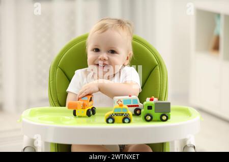 Giocattoli per bambini. Bambino carino che gioca con le macchinine giocattolo in seggiolone a casa Foto Stock