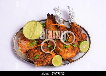 Il pollo Tandoori è arrosto, marinato nello yogurt e speziato generosamente, donando alla carne un colore rosso guarnito con cipolla, limone e chutney verde Foto Stock