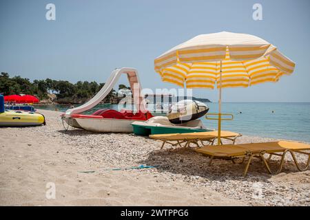 Un'area relax sulla spiaggia. Due chaise longue con materassi morbidi si stendono sulla sabbia all'ombra di un ombrellone. Vicino a loro c'è acqua bi Foto Stock