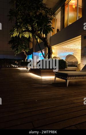 Edificio moderno dall'esterno di notte. Immagine notturna della piscina e dell'edificio del resort in stile condominiale con sedie a sdraio lungo il lato della piscina. Foto Stock