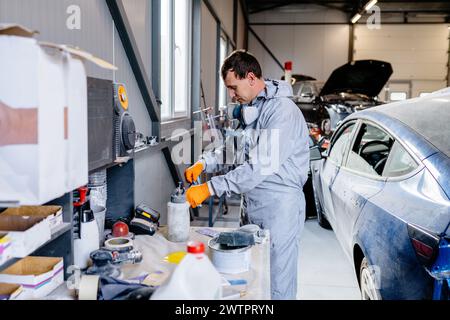 Il personale addetto alla riparazione versa la vernice rossa nella pistola a spruzzo presso l'officina di verniciatura carrozzeria del centro di assistenza auto. Foto Stock