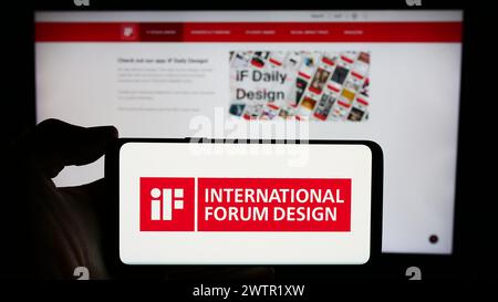 Persona che detiene un cellulare con il logo dell'organizzazione tedesca International Forum Design (IF) di fronte alla pagina web aziendale. Mettere a fuoco il display del telefono. Foto Stock