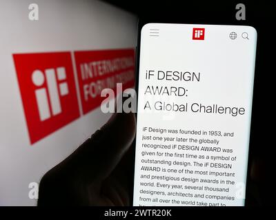 Persona che possiede uno smartphone con pagina web dell'organizzazione tedesca International Forum Design (IF) davanti al logo. Messa a fuoco al centro del display del telefono. Foto Stock