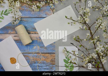 Ramoscelli in fiore con fiori bianchi, foglie dipinte e foglio di carta vuoto per riempire il contenuto su sfondo in legno, vista dall'alto. Primavera. Foto Stock