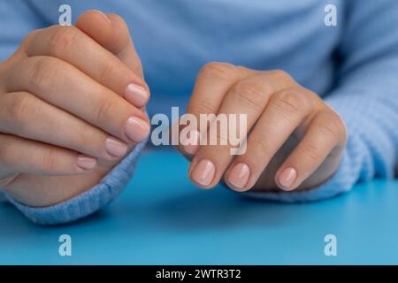 Unghie pastello morbide e curate su sfondo blu. Donna che mostra la sua nuova manicure nei colori della tavolozza pastello. Decorazioni semplici, fresche vibrazioni primaverili dai colori naturali Foto Stock