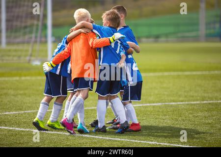 Happy Boys Jumping e Huddling celebrano la partita vincente. I bambini della squadra di calcio giocano il torneo Foto Stock