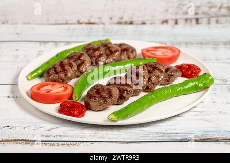 Polpette di carne alla griglia. Polpette grigliate turche con peperoni arrostiti e pomodori su fondo in legno Foto Stock