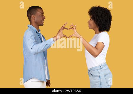 Profilo laterale di una coppia afroamericana sorridente che forma una forma a cuore con le mani unite Foto Stock