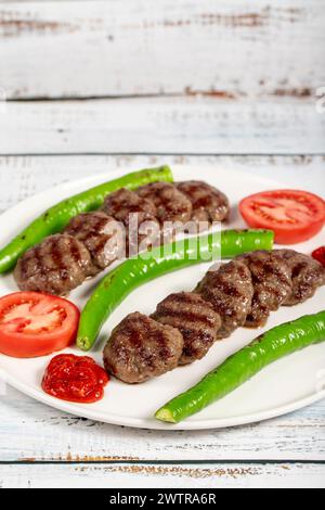 Polpette di carne alla griglia. Polpette grigliate turche con peperoni arrostiti e pomodori su fondo in legno Foto Stock