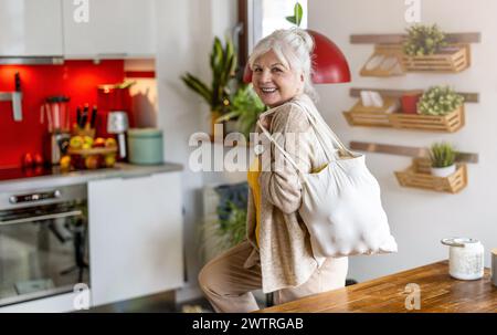 Donna anziana che tiene in mano una borsa riutilizzabile con alimentari in cucina Foto Stock