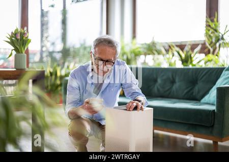 Uomo anziano che utilizza lo smartphone per configurare un purificatore d'aria domestico Foto Stock