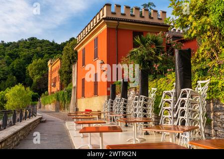 Tavoli da caffe' all'aperto su un argine con colorata villa sul lago di Como in ristorante all'aperto senza nessuno, Lenno comune, Lombardia, Italia. Viaggi popolari Foto Stock